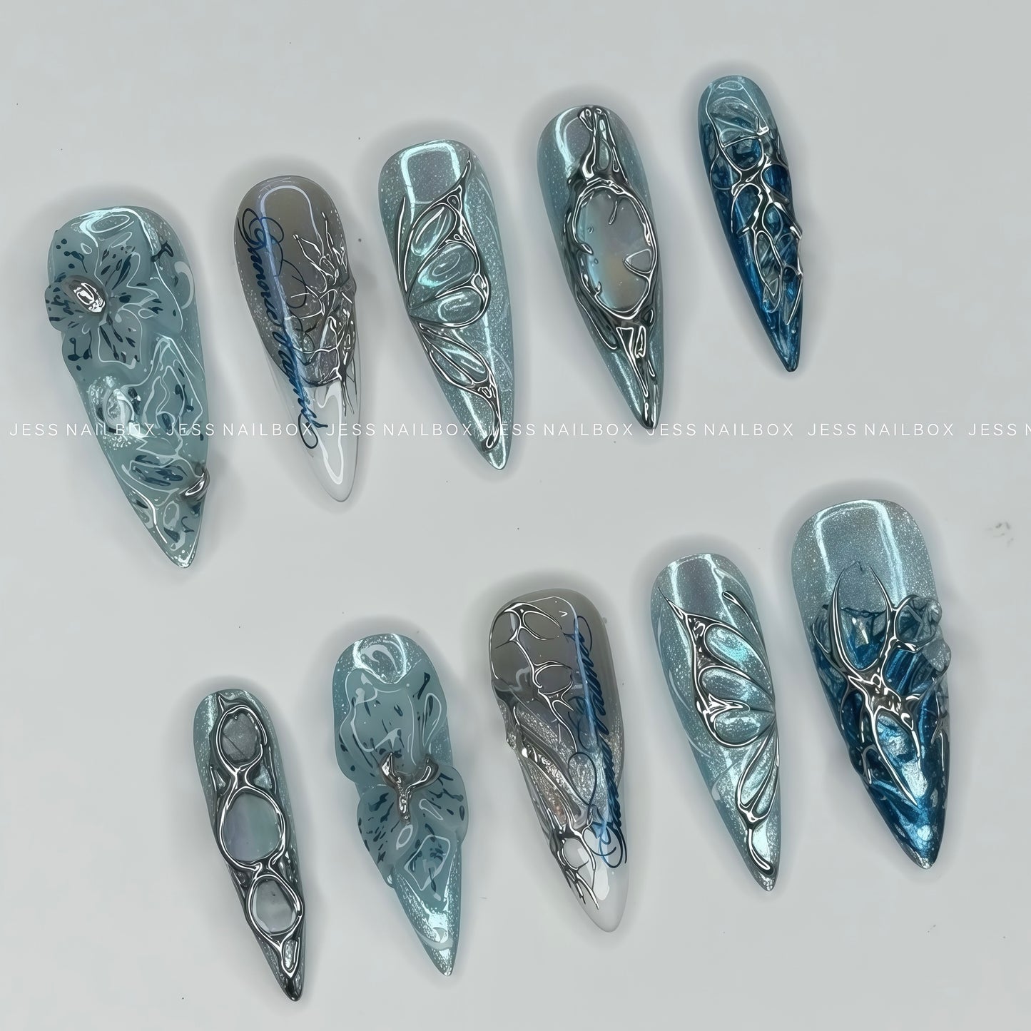 Handcrafted Frost Flora ice blue press on nails featuring 3D liquid chrome filigree, cyber butterfly accents, and cat eye shimmer in long stiletto shape 45 degree.