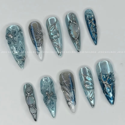 Handcrafted Frost Flora ice blue press on nails featuring 3D liquid chrome filigree, cyber butterfly accents, and cat eye shimmer in long stiletto shape 45 degree.