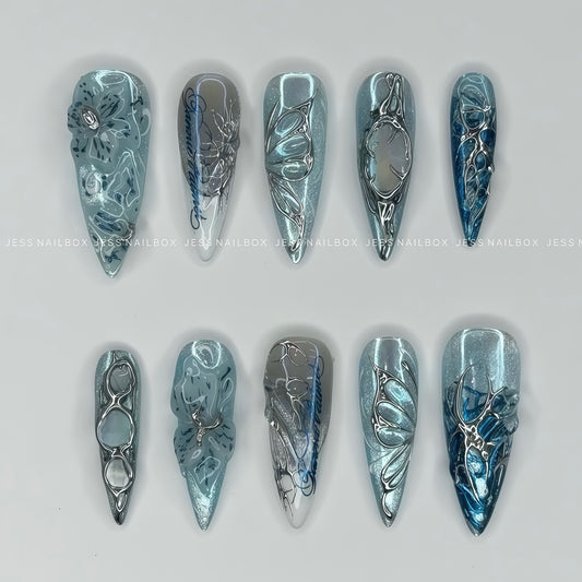 Handcrafted Frost Flora ice blue press on nails featuring 3D liquid chrome filigree, cyber butterfly accents, and cat eye shimmer in long stiletto shape.
