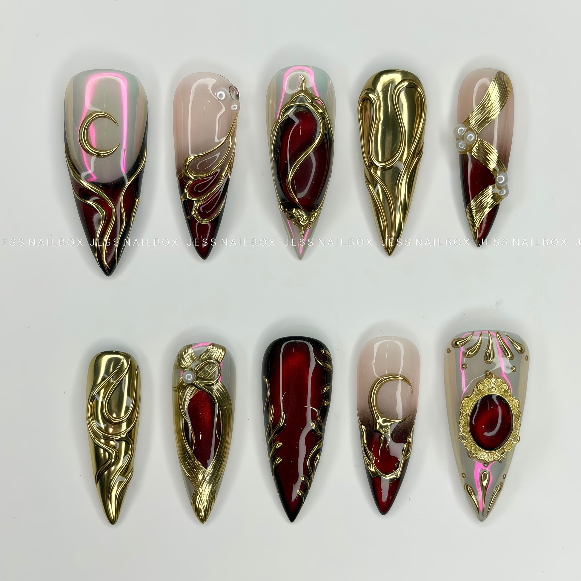 Stiletto press-on nails featuring a deep red cat-eye gel illusion, gold liquid metal baroque frames, and crescent moon details on an ombre base.